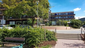 A multi-story building with a modern design, a paved walkway, and a bench in a landscaped area.
