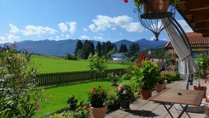 A patio with a wooden table, potted plants, and a hanging flower basket. - Cozy Alpine Flat in Altenau (Saulgrub)