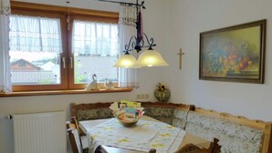 A dining area with a wooden table and chairs, a window with curtains, a radiator, and a wall-mounted cross.