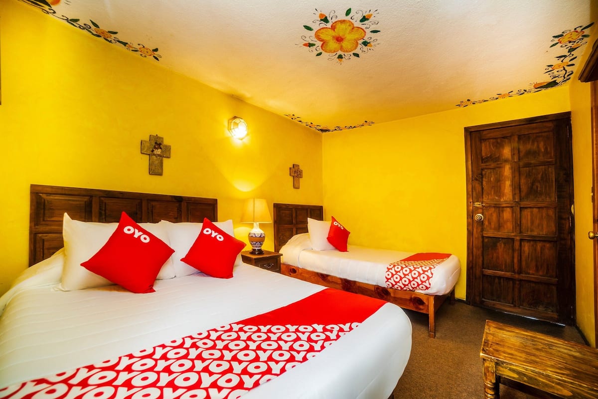 Habitació d'hotel amb dos llits, cadascun amb roba de llit vermella i blanca, un capçal de llit de fusta, una tauleta de nit amb una làmpada i una porta de fusta.