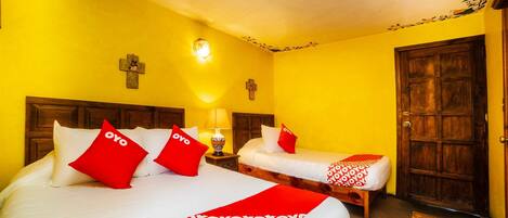 A hotel room with two beds, each with red and white bedding, a wooden headboard, a nightstand with a lamp, and a wooden door.