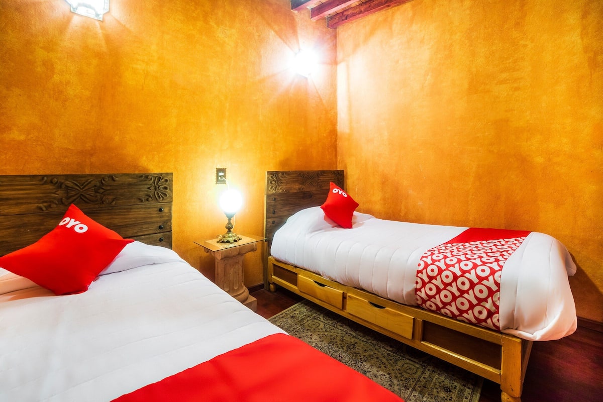 Habitació d'hotel amb dos llits, cada un amb un llençol i almoines vermelles i blanques a joc. Hi ha una meseta de nit amb una làmpada entre els llits.