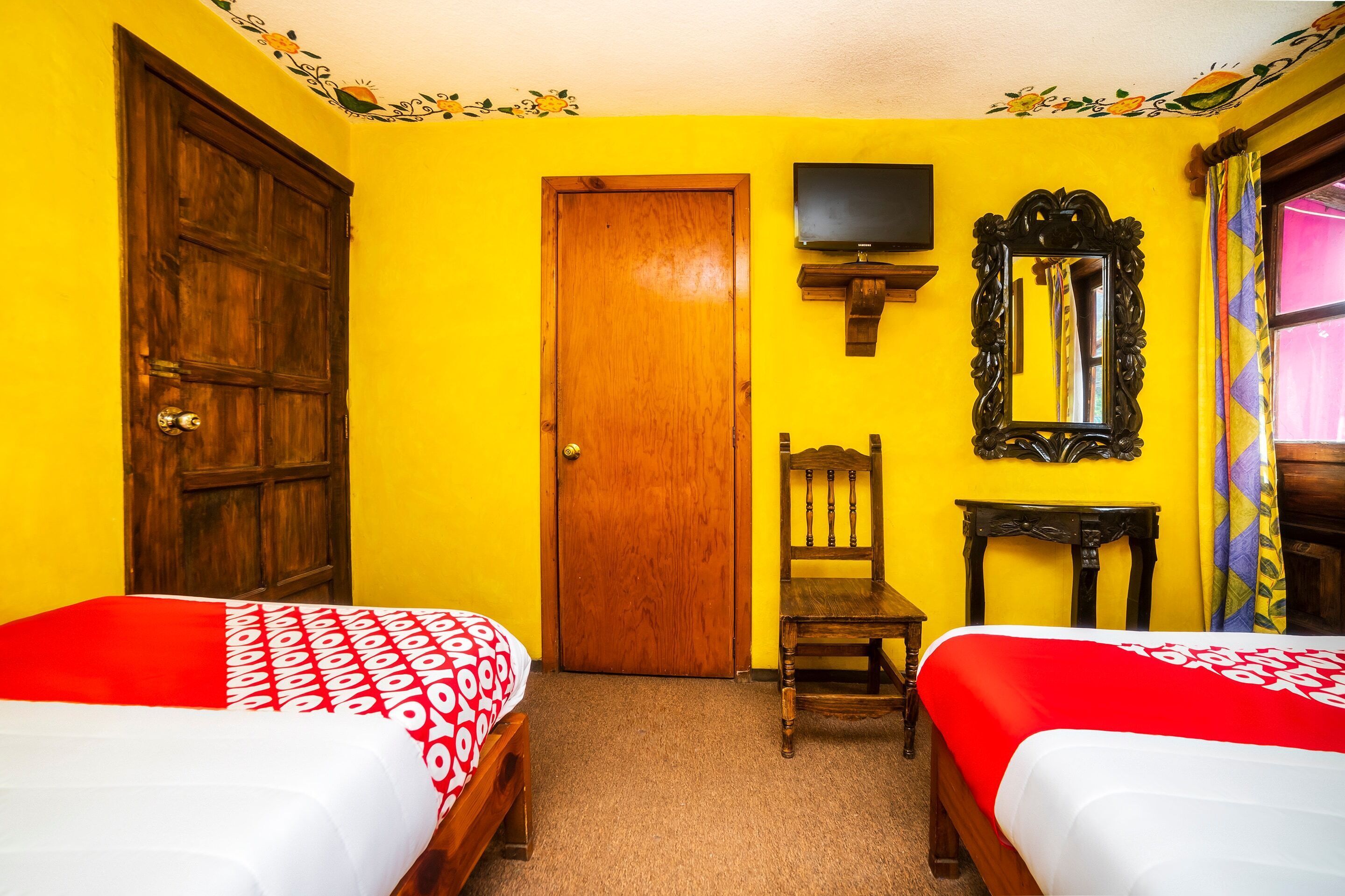 A room with two beds, a wooden door, a television, a mirror, and a chair.