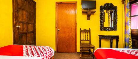 A room with two beds, a wooden door, a television, a mirror, and a chair.