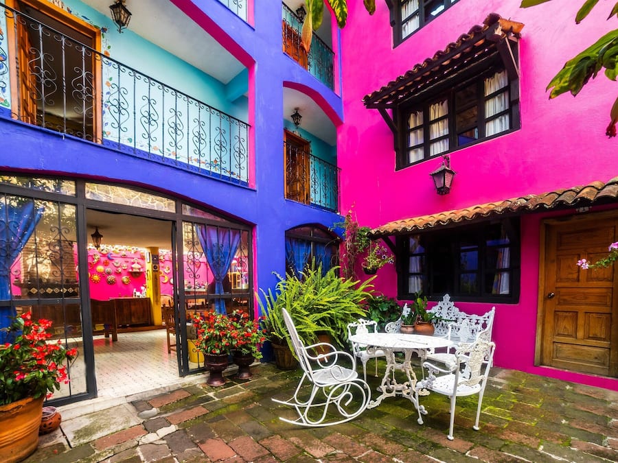 A courtyard with a white rocking chair and table, surrounded by colorful buildings with balconies and potted plants.