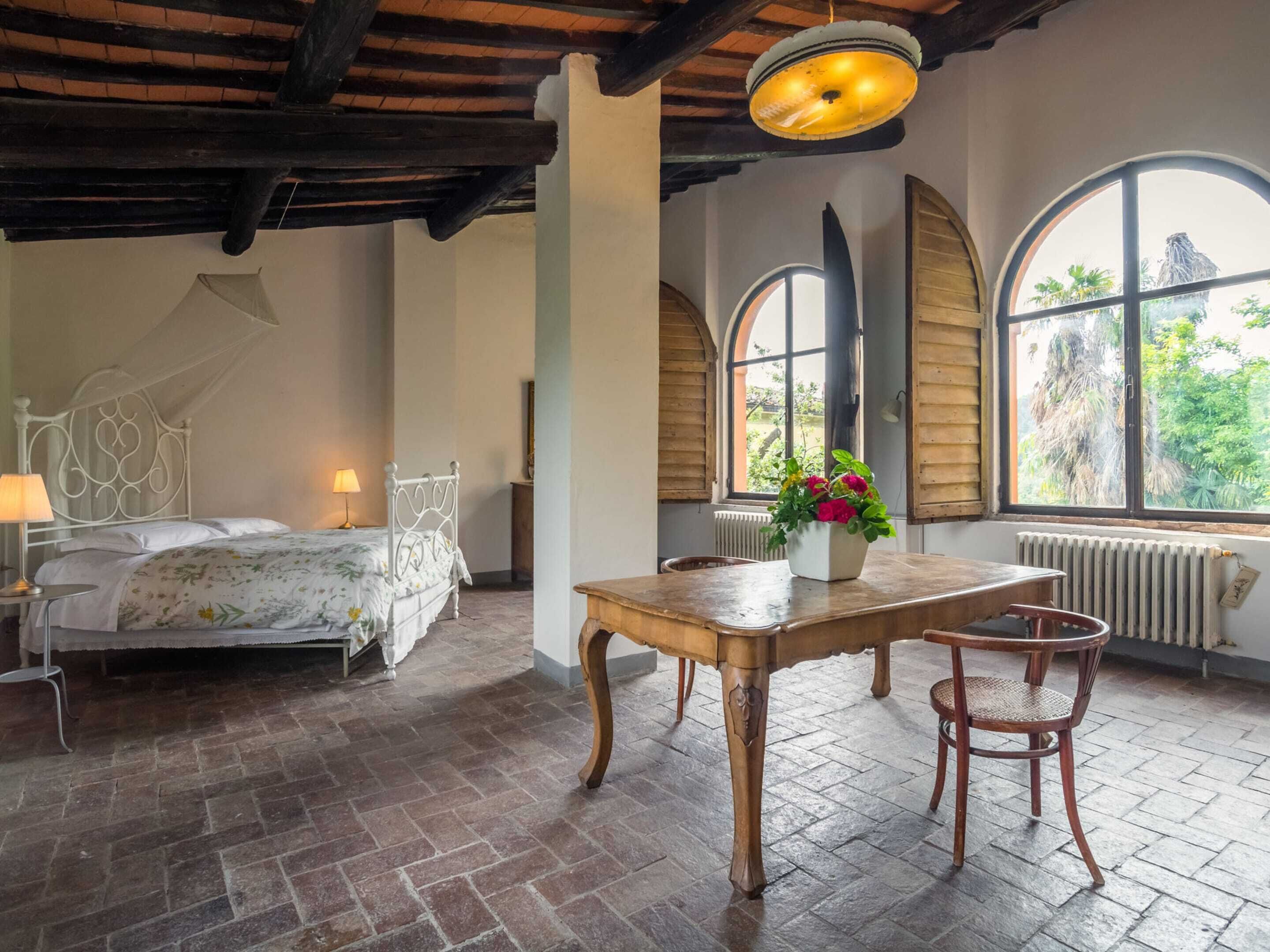 Une chambre à coucher avec un lit, une table en bois avec des chaises, une fenêtre avec des volets et un radiateur.