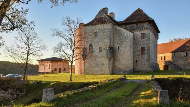 En historisk byggnad i sten med ett markant torn, en stenlagd gångväg och en gräsyta.