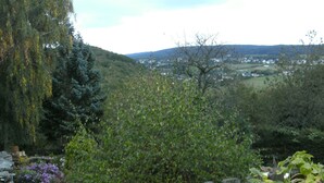 A garden with a wooden fence, a bench, and a view of a valley with houses in the distance. - Apartment in Morbach Near Ski Lift (Morbach)