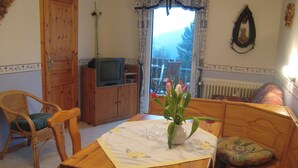 A cozy living room with a wooden table, chairs, a television, and a window with a view of trees. - Apartment in Morbach Near Ski Lift (Morbach)