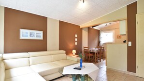 A living room with a beige sofa, a glass coffee table with a turtle sculpture, and a dining area with wooden chairs and a table. - Quaint Bungalow with Garden near Insel Poel (Insel Poel)