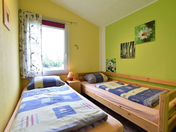 Une chambre avec deux lits simples, une fenêtre avec des rideaux, une lampe et des œuvres d’art murales.