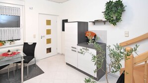 Una cocina moderna con armarios blancos, encimera negra y horno empotrado. Se ve una ventana con cortinas blancas y una planta en maceta sobre el alféizar.