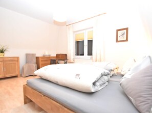 A bedroom with a bed, a desk, a chair, a radiator, a window with curtains, and a framed picture on the wall. - Cosy Apartment in the Harz Mountains (Nordhausen)
