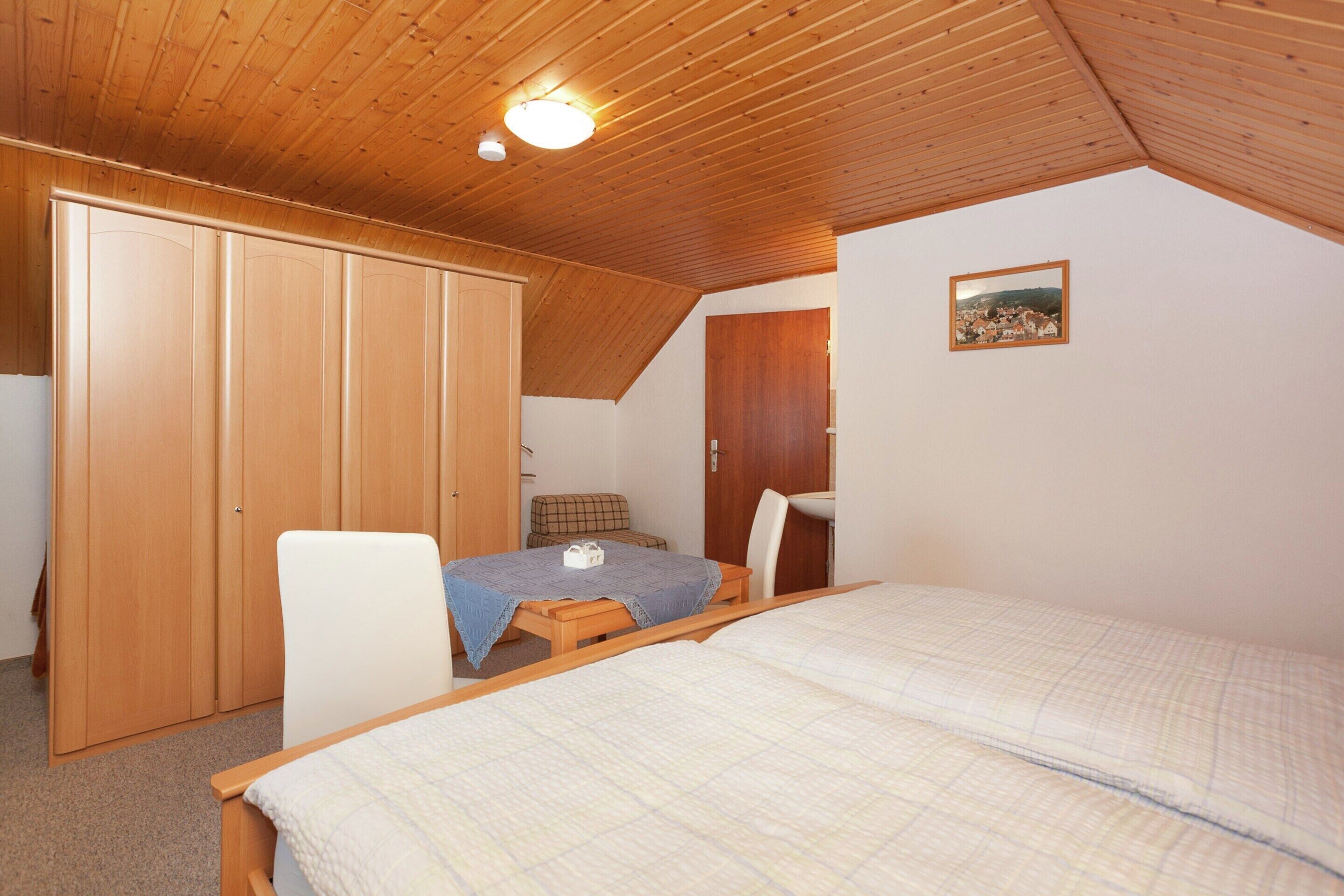 A bedroom with a wooden ceiling, a bed, a desk, a chair, and a wardrobe.