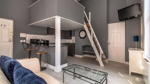 Una sala de estar moderna con un sofá, una mesa de centro de vidrio y una zona de cocina con una escalera.