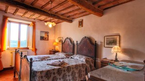 Une chambre à coucher avec deux lits en bois, une commode en bois, une fenêtre avec des rideaux et un plafond avec des poutres apparentes.