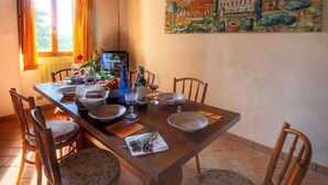 Un coin repas avec une table en bois dressée pour quatre personnes, des chaises, un tableau accroché au mur et une fenêtre avec des rideaux.