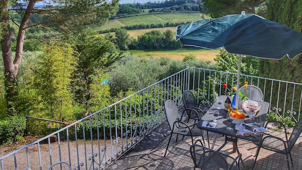 Une terrasse extérieure avec une table dressée pour le repas, entourée d’une clôture en métal et offrant une vue panoramique sur la campagne environnante.