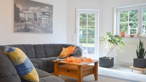 A living room with a grey sofa, a wooden coffee table, and a large window with a view of greenery. - Beautiful Holdiday Home in Ulmen Near the Lake (Ulmen)