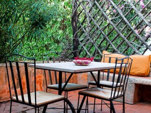 An outdoor seating area with a table and chairs, surrounded by a lattice fence and lush greenery. - Home in Sardinia Near Spiaggia Li Canneddi (Trinità d'Agultu e Vignola)