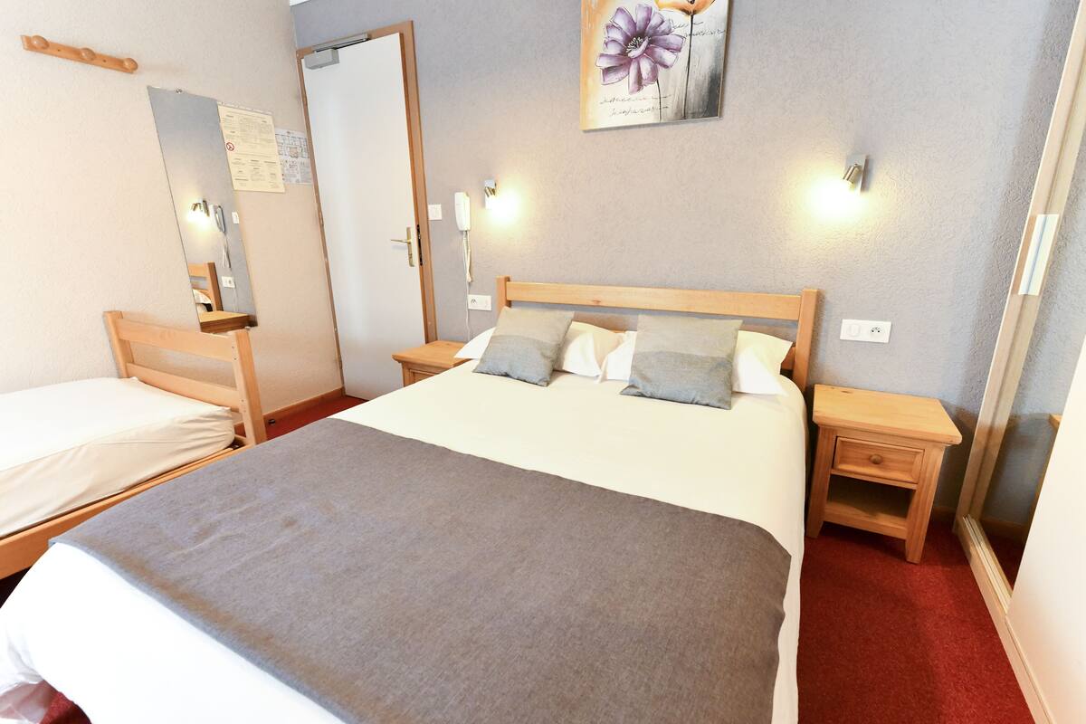 Habitación de hotel con una cama grande, dos mesitas de noche, un cabecero de madera, un espejo y una lámpara fijada a la pared.