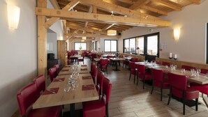 Un restaurant spacieux avec des poutres en bois, des chaises rouges et des tables soigneusement dressées.
