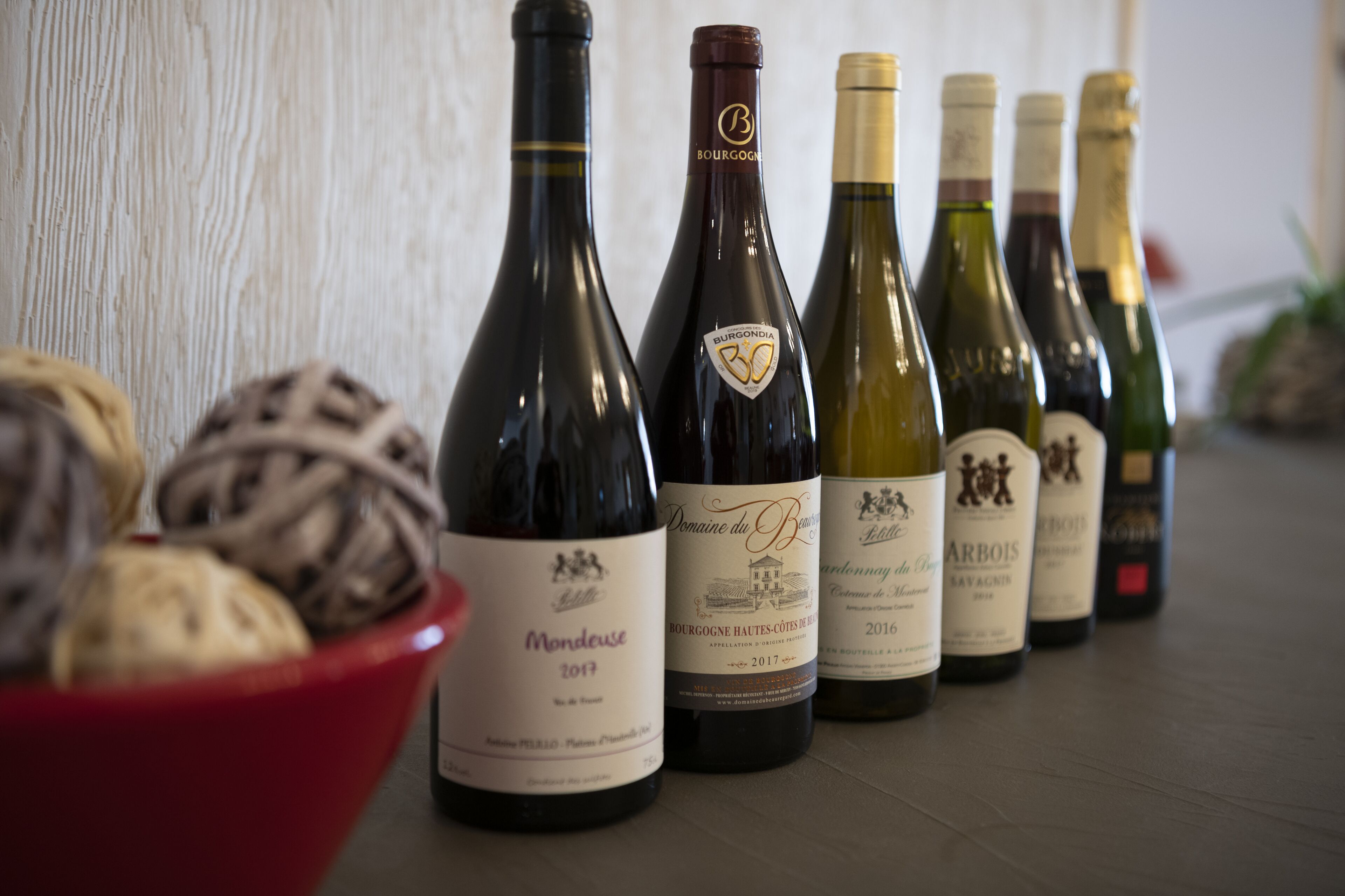 Une rangée de bouteilles de vin est posée sur une table, avec un panier de pain en premier plan.