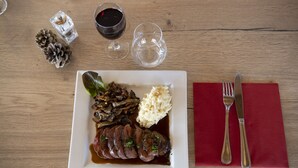Une assiette carrée blanche, sur laquelle on voit de la viande en tranches, des champignons et de la purée de pommes de terre, le tout posé sur une table en bois.
