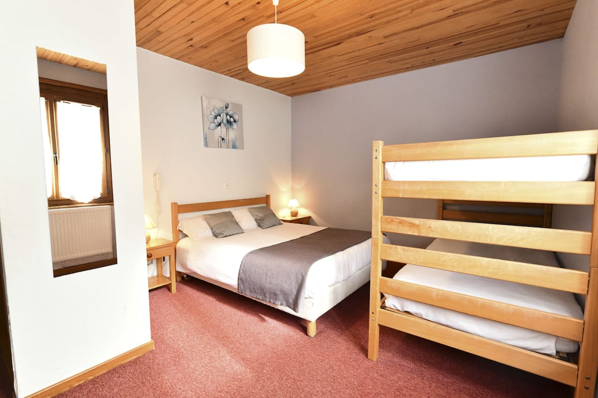 Un dormitorio con una cama litera, una cama individual, techo de madera, radiador, un cuadro y una mesita de noche con lámpara.