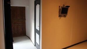 Un pasillo con una puerta de madera, un televisor montado en la pared y una puerta con marco negro.