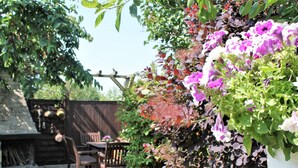 A garden with a wooden table and chairs, a brick oven, and a climbing plant with purple flowers. - Klutz Garden Apartment (Klütz)