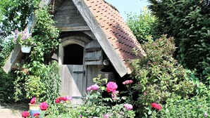 A rustic wooden structure with a sloped roof, surrounded by lush greenery and blooming pink flowers. - Klutz Garden Apartment (Klütz)