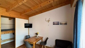 A room with a wooden ceiling, a TV mounted on the wall, a table with chairs, a sofa, and a small table with a vase. - Klutz Garden Apartment (Klütz)
