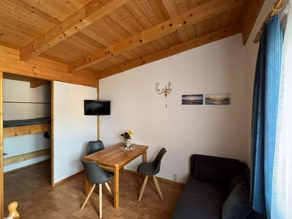 Une pièce avec un plafond en bois, un téléviseur fixé au mur, une table avec des chaises, un canapé et une petite table sur laquelle est posé un vase.