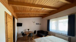 A room with a wooden ceiling, a bed, a sofa, a dining table with chairs, and a TV mounted on the wall. - Klutz Garden Apartment (Klütz)