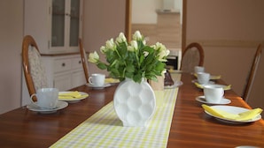 A dining table with a vase of white roses, white cups, and a checkered table runner. - Group Stay in Ulmen-furth (Ulmen)