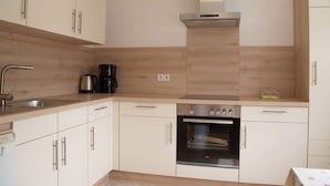 A modern kitchen with white cabinets, a stainless steel range hood, a coffee maker, and an oven. - Group Stay in Ulmen-furth (Ulmen)