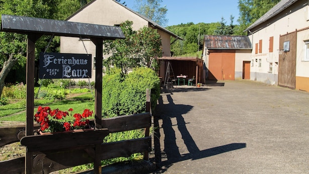 A building with a sign reading "Ferienhaus Lutz" and a wooden bench with red flowers. - Group Stay in Ulmen-furth (Ulmen)
