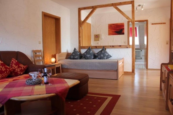 A cozy room with a bed, a table with a red and white checkered tablecloth, a wooden-framed mirror, and a red rug. - Pleasing Apartment in Herrischried near Forest (Herrischried)