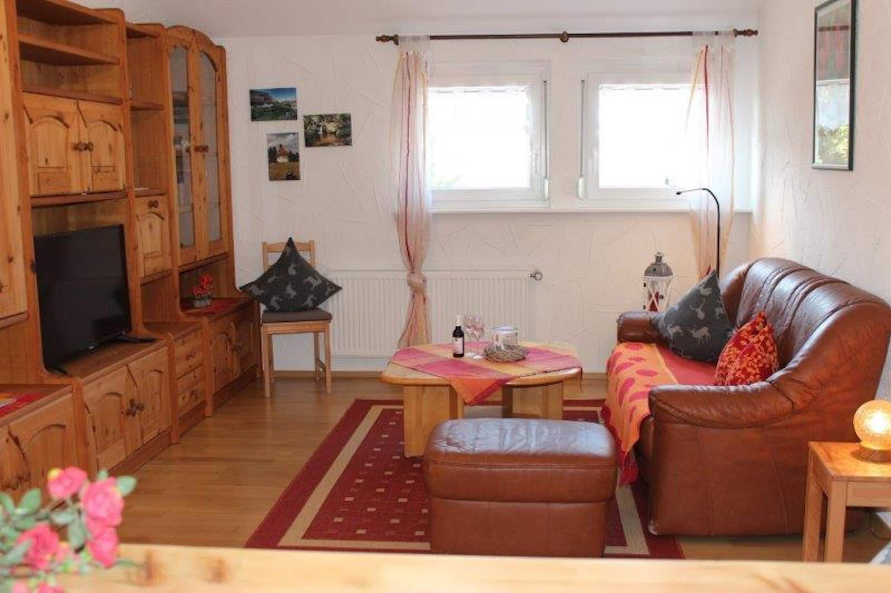 A cozy living room with a brown leather sofa, a wooden cabinet with a TV, a small round table with a candle, and a window with curtains.
