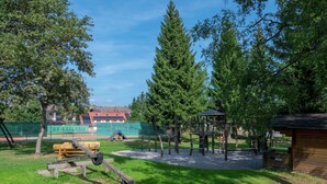 A playground with climbing structures and a slide, surrounded by trees and a building in the background.