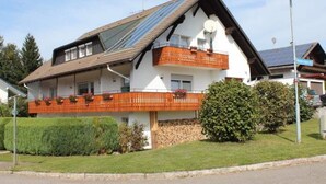 A two-story house with a sloped roof, solar panels, and a balcony with orange railings.