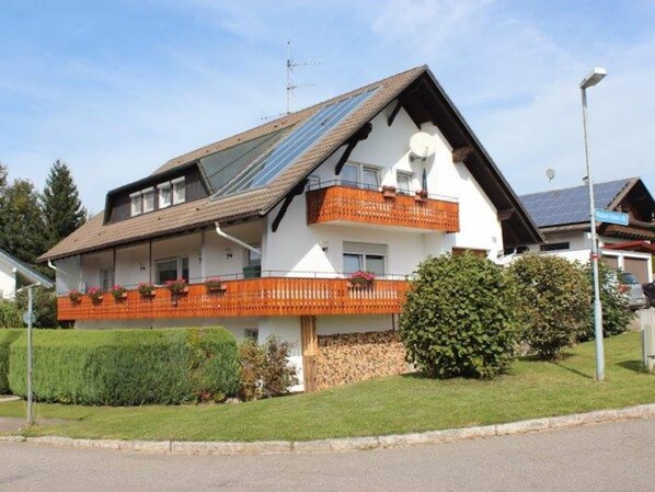 Une maison à deux étages, dotée d’un toit en pente, de panneaux solaires et d’un balcon avec des rampes orange.