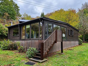 A single-story wooden house with a covered porch and a staircase leading to the entrance. - Maboge Cottage With Garden (La Roche-en-Ardenne)