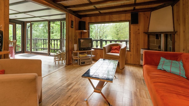 Interno di una baita in legno con un divano, una televisione, un tavolo e un camino.
