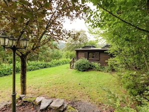 A rustic cabin with a wooden exterior, a stone pathway leading to it, and a lush green garden. - Maboge Cottage With Garden (La Roche-en-Ardenne)