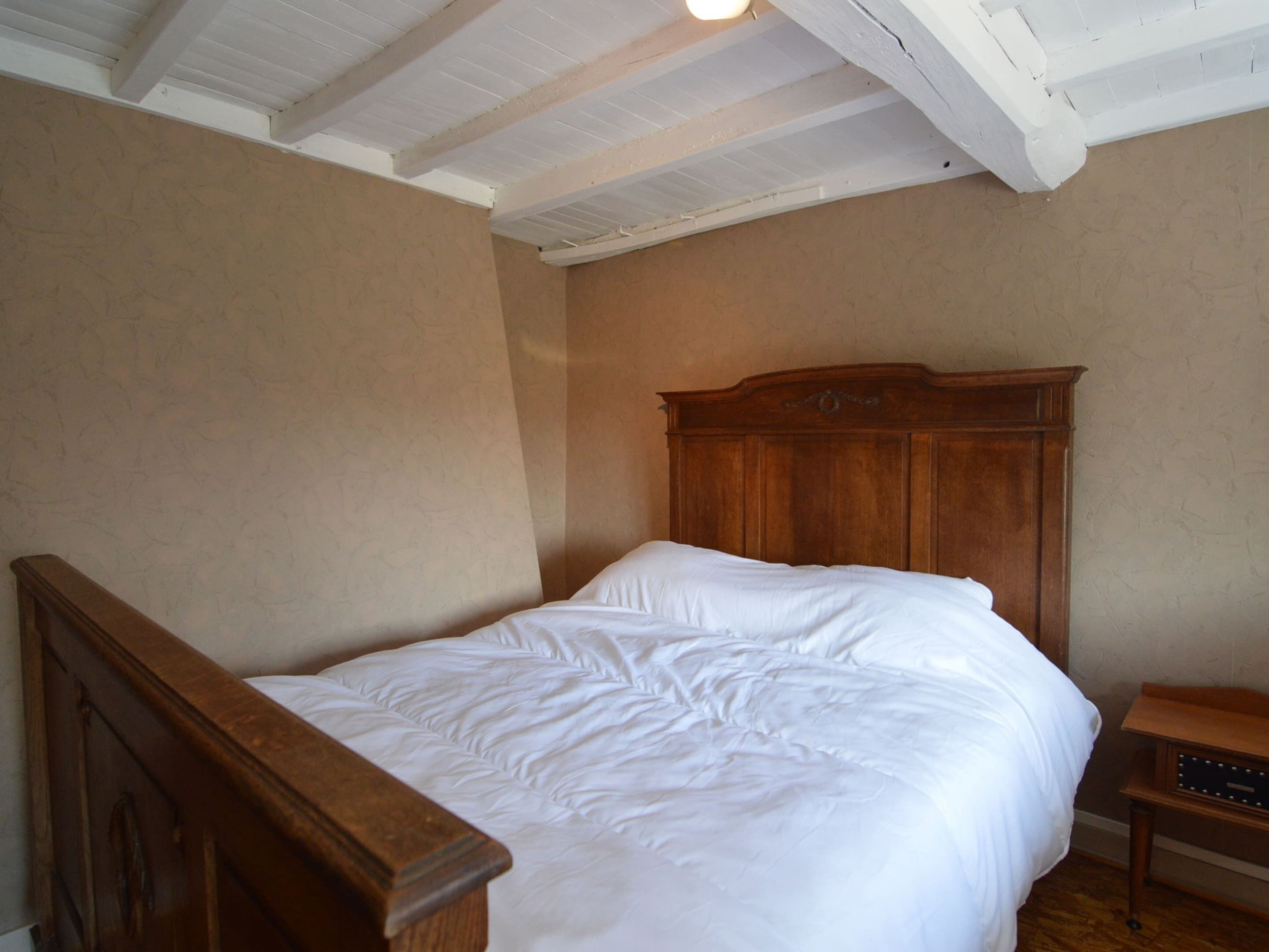 A bedroom with a wooden bed, white bedding, and a wooden nightstand.