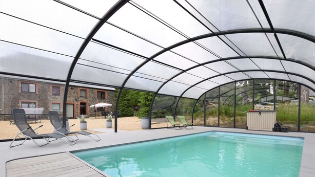 A covered swimming pool with lounge chairs and a stone building in the background. - Cottage in Ardennes With Heated Pool (La Roche-en-Ardenne)