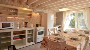 A kitchen with a dining area, featuring a table set for four, a microwave, a coffee maker, and a refrigerator. - Cottage in Ardennes With Heated Pool (La Roche-en-Ardenne)
