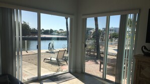 Et værelse med en stor skydedør, der fører til en udendørs terrasse med pool, stole og udsigt over vandet.
